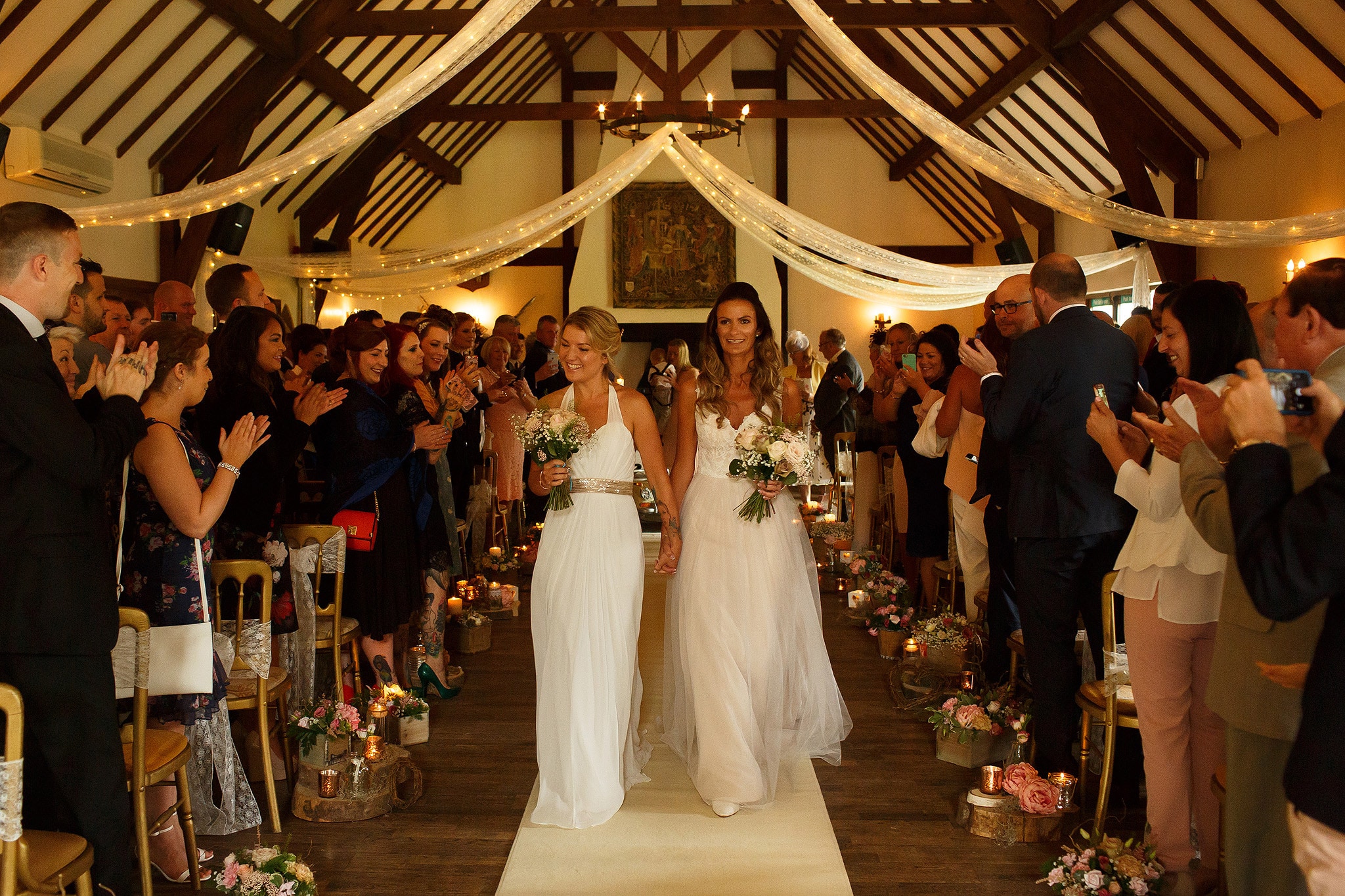 Newlywed brides walking down the aisle together smiling - great hall at mains wedding photography