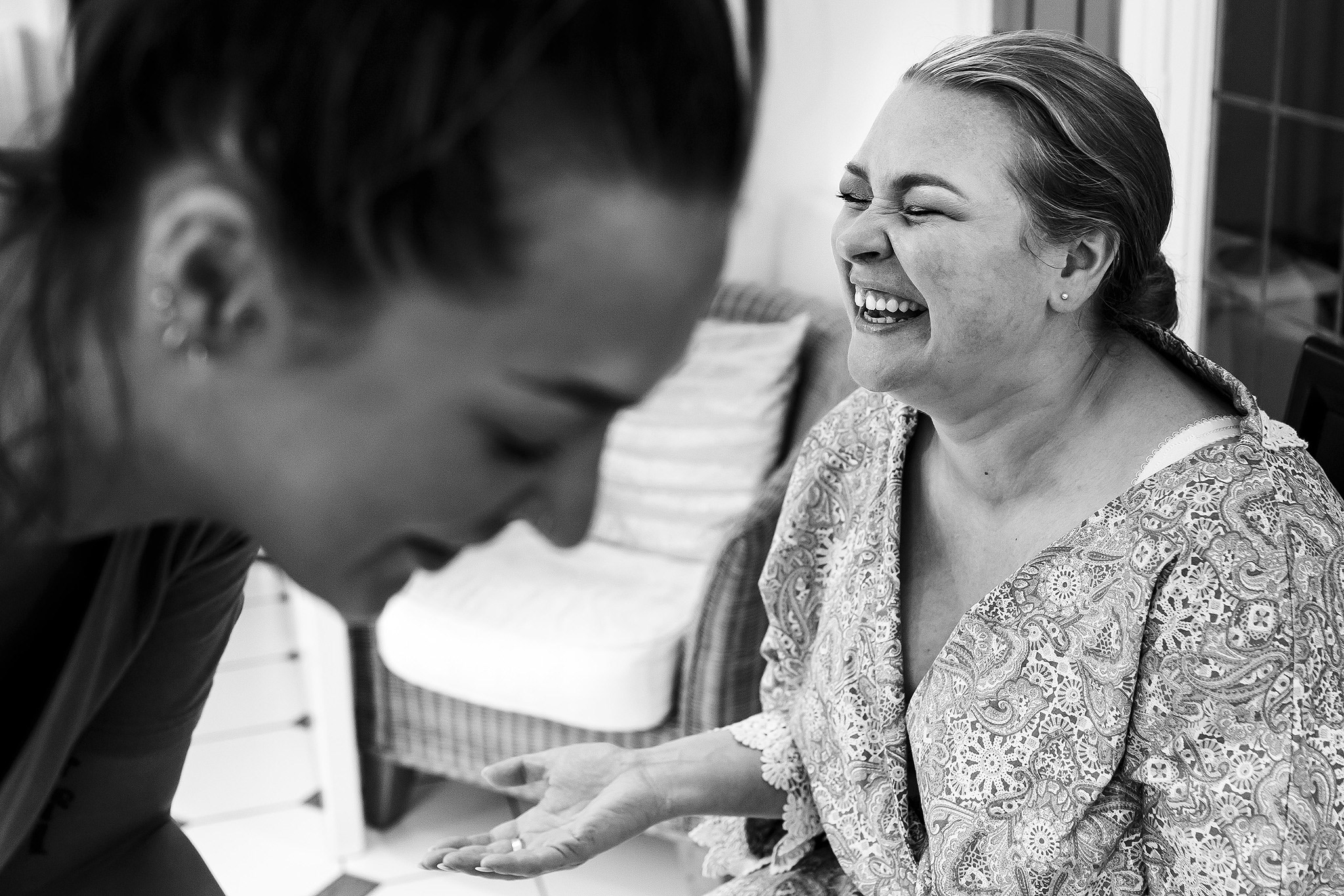 Black and white image of the bride laughing on the morning of her wedding whilst having make up applied