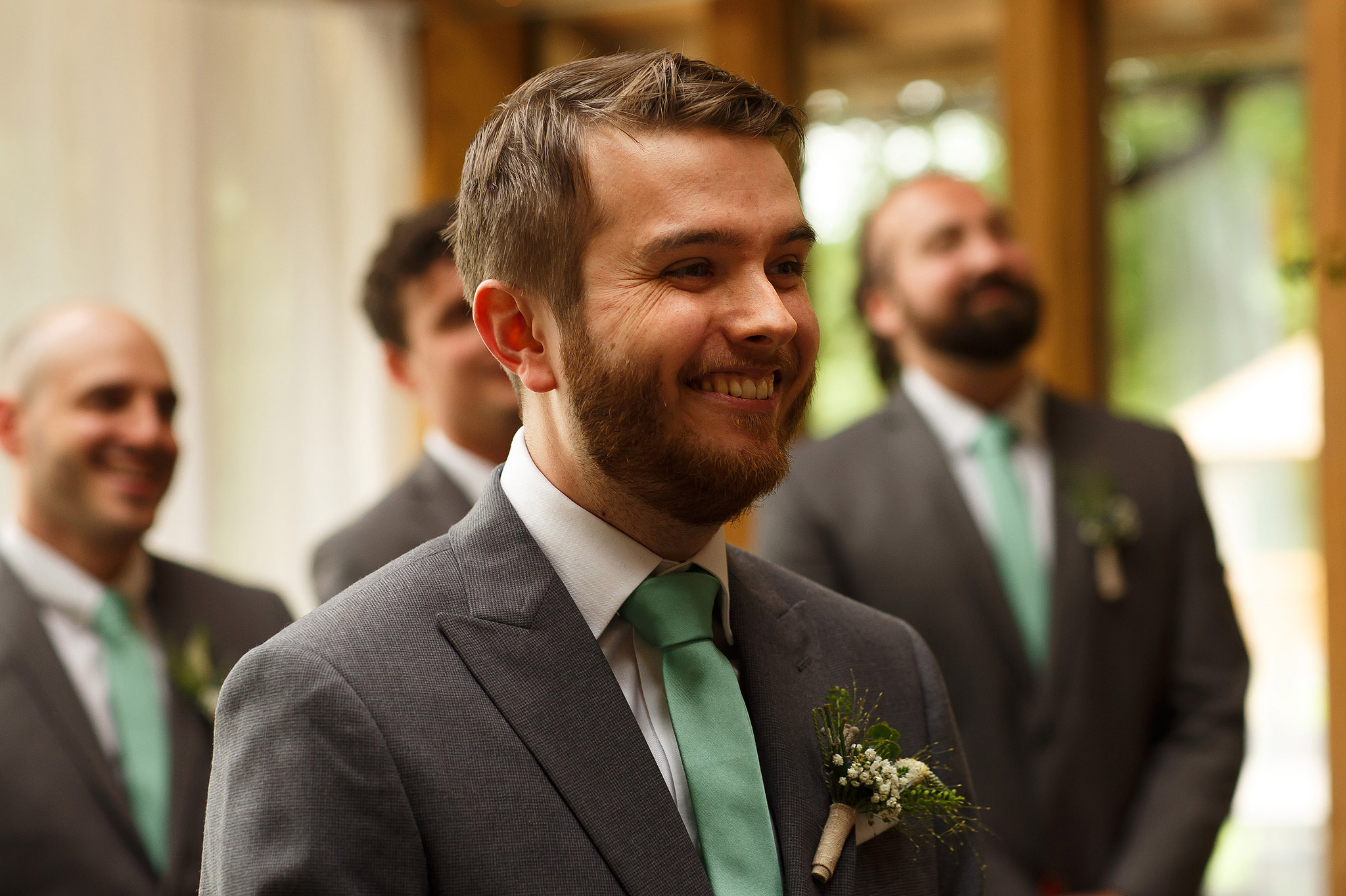 Groom wearing grey suit and mint green tie smiling as he sees bride for the first time
