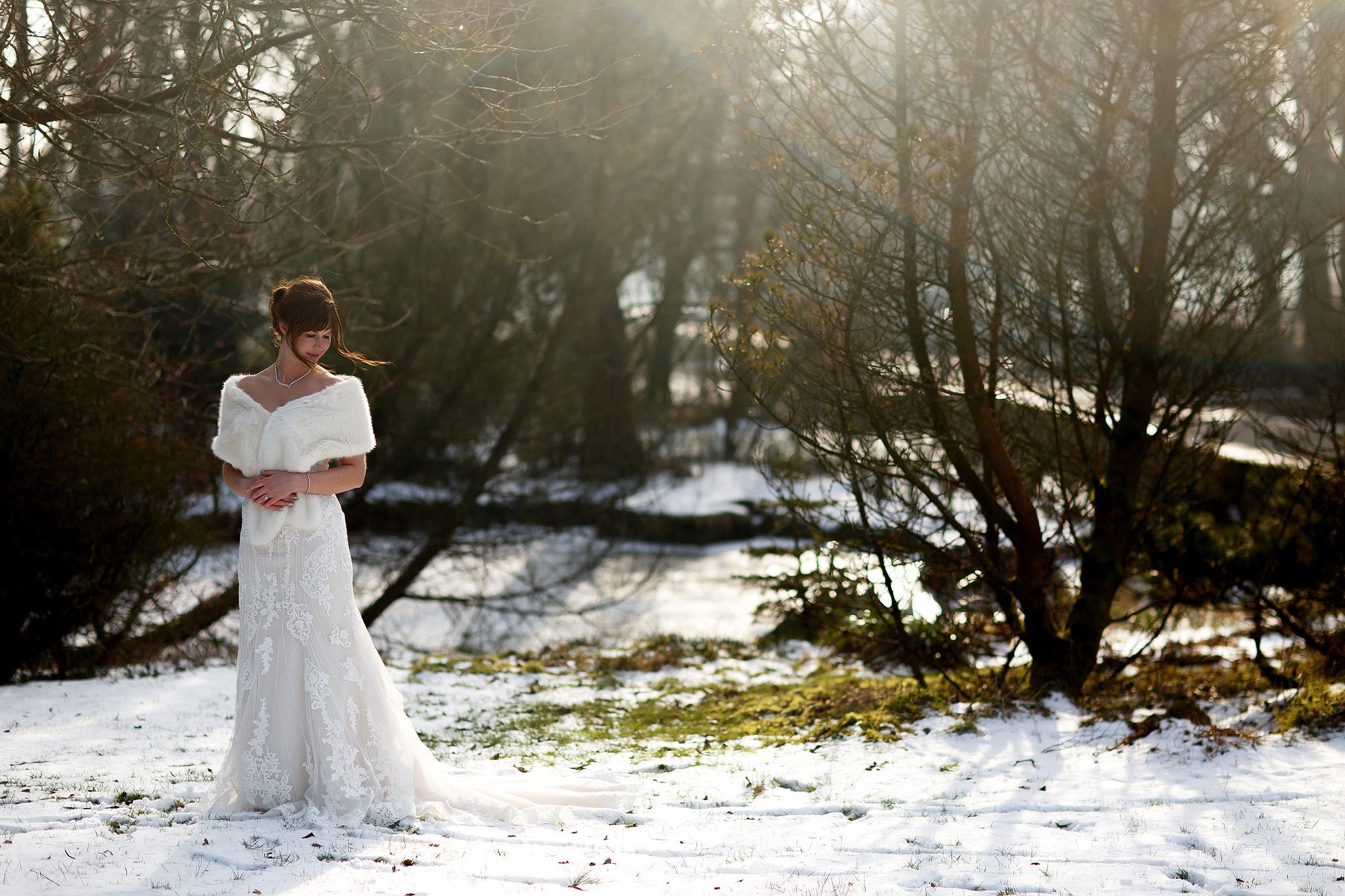 Bridal wearing strapless lace wedding dress and fur shrug looking to the snowy ground during winter wedding at Rivington Hall Barn