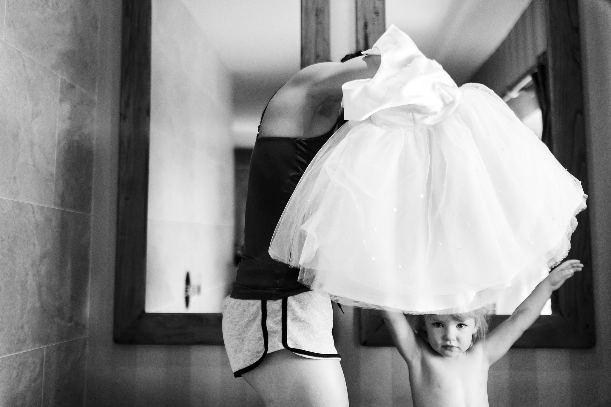 Flower girl holding arms high as bride looks to put her dress on over her head