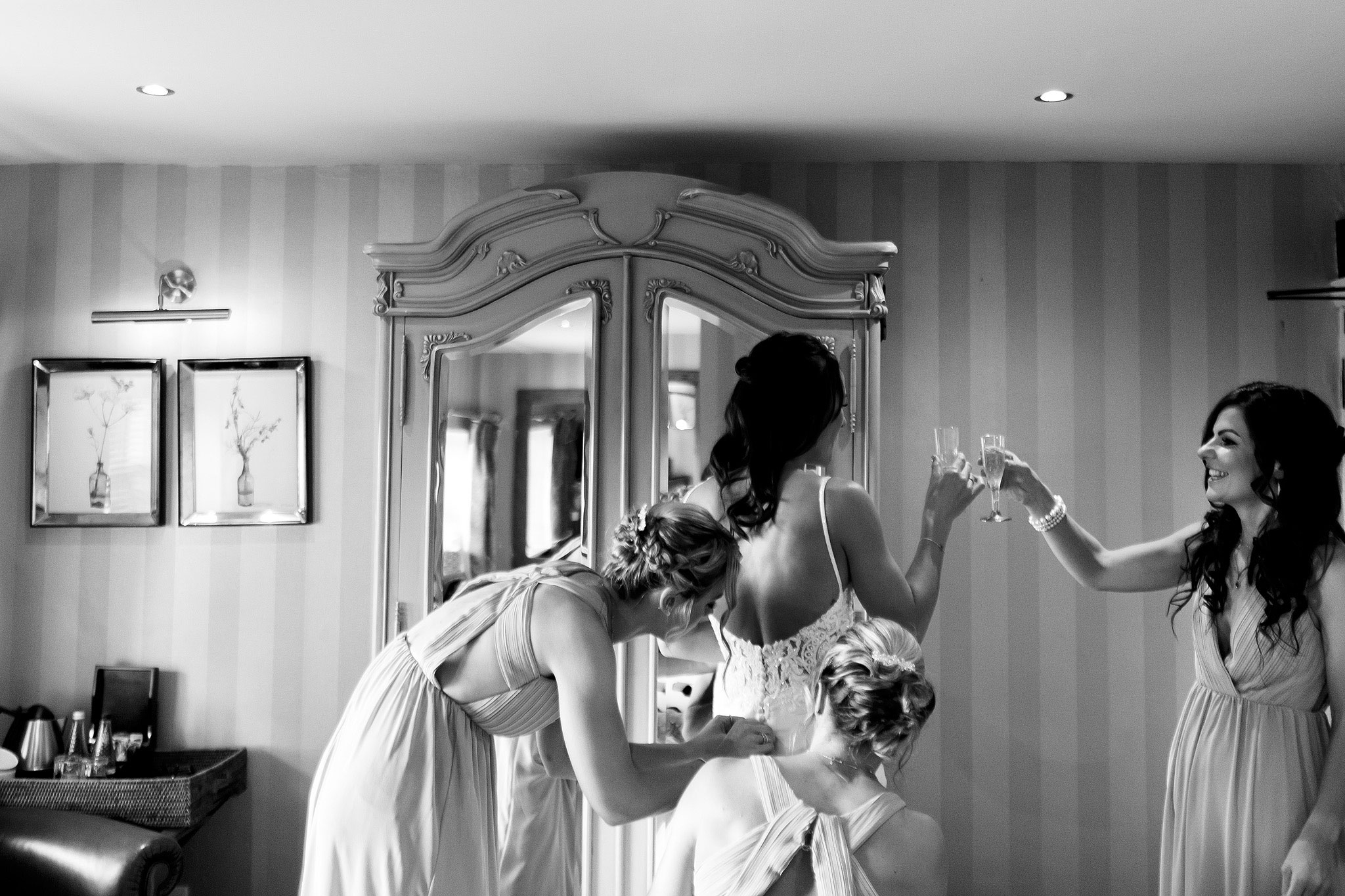 Bride toasting bridesmaid as her dress is nearly fastened 
