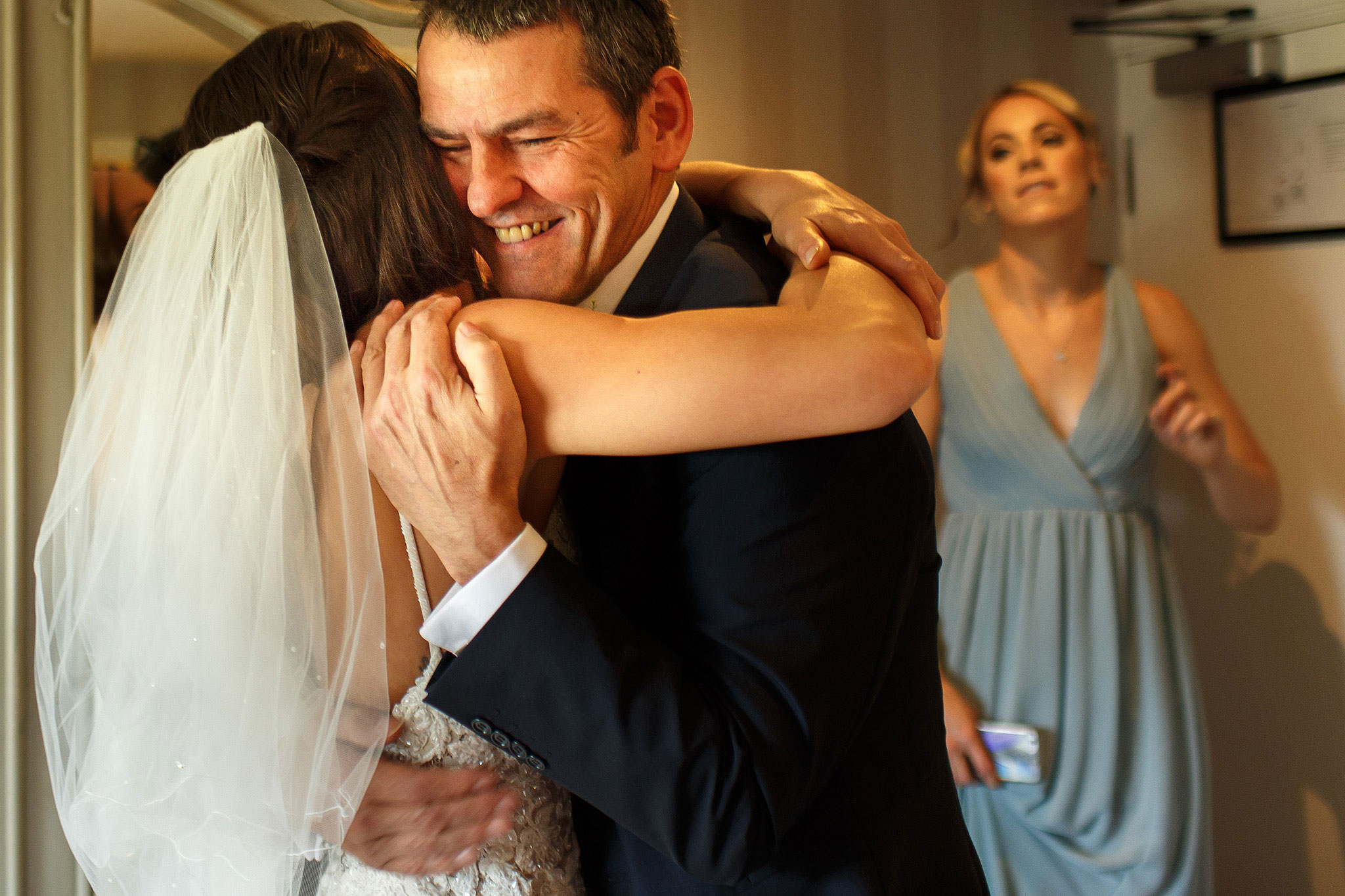 Father of the bride hugging bride as he sees her in her dress for the first time