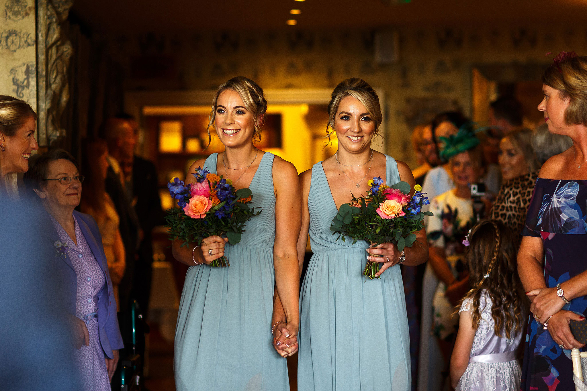 Bridesmaids with colourful flowers walking down the aisle wearing long pale blue dresses