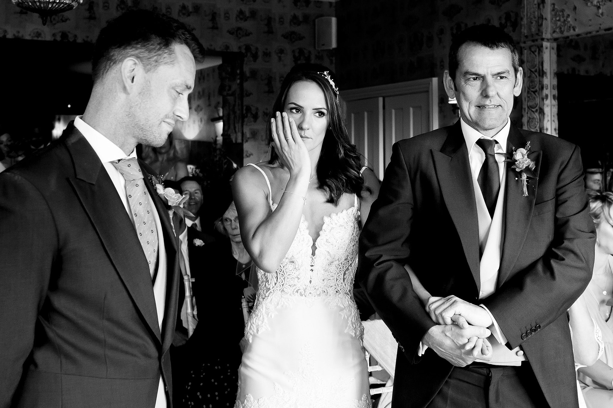 Bride delicately holding her hand to her face holding back tears as she reached her groom at the top of the aisle