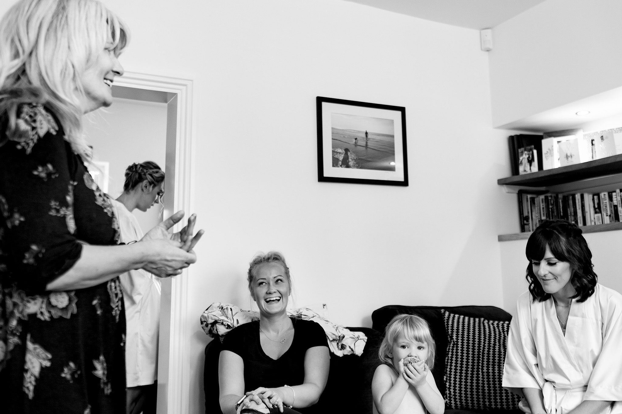 Documentary scene setting image of bridal party sat on the sofa laughing