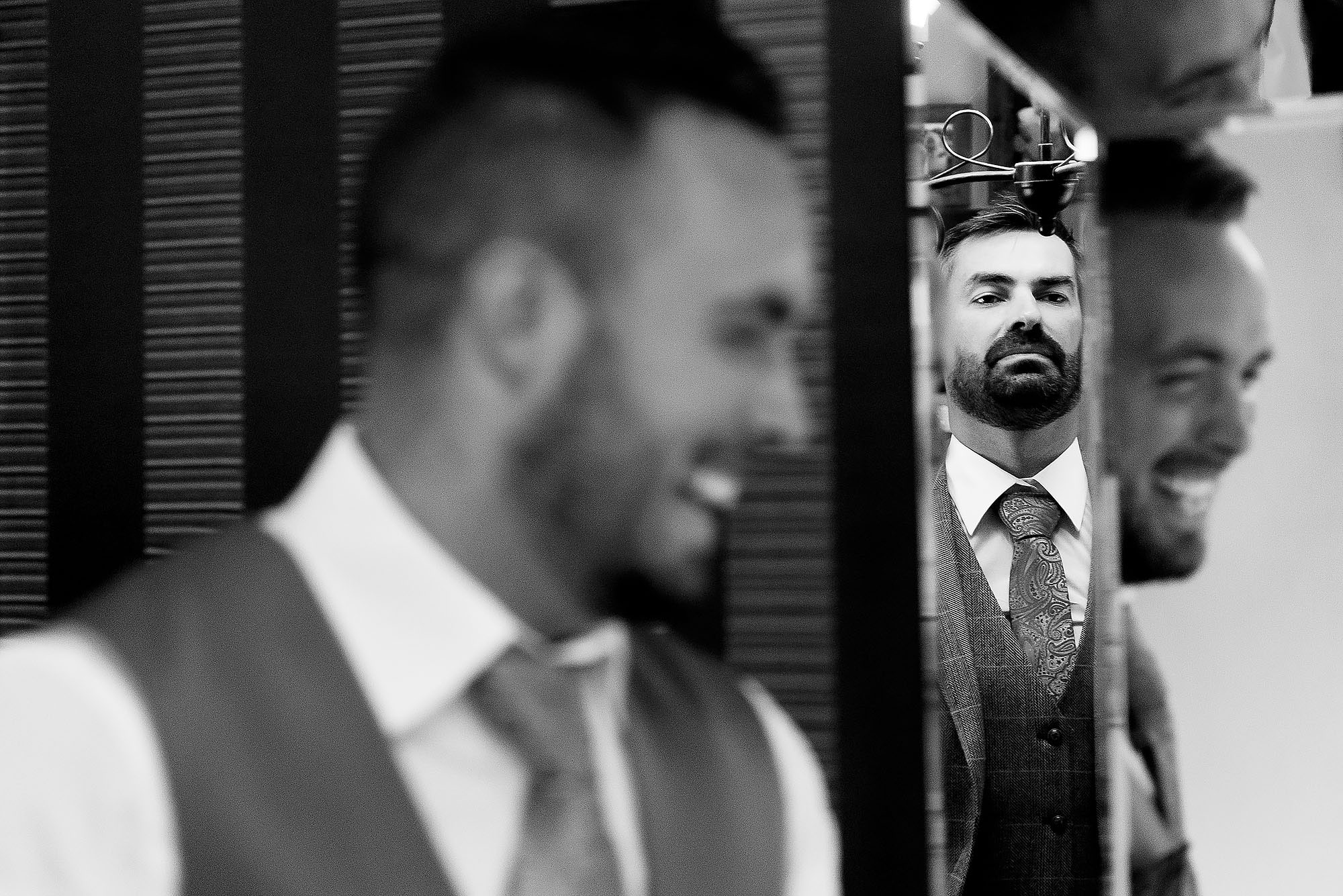 Groom with beard wearing tweed waistcoat and paisley tie looking into mirror on wedding morning | Wellbeing Farm wedding photographs by Toni Darcy Photography