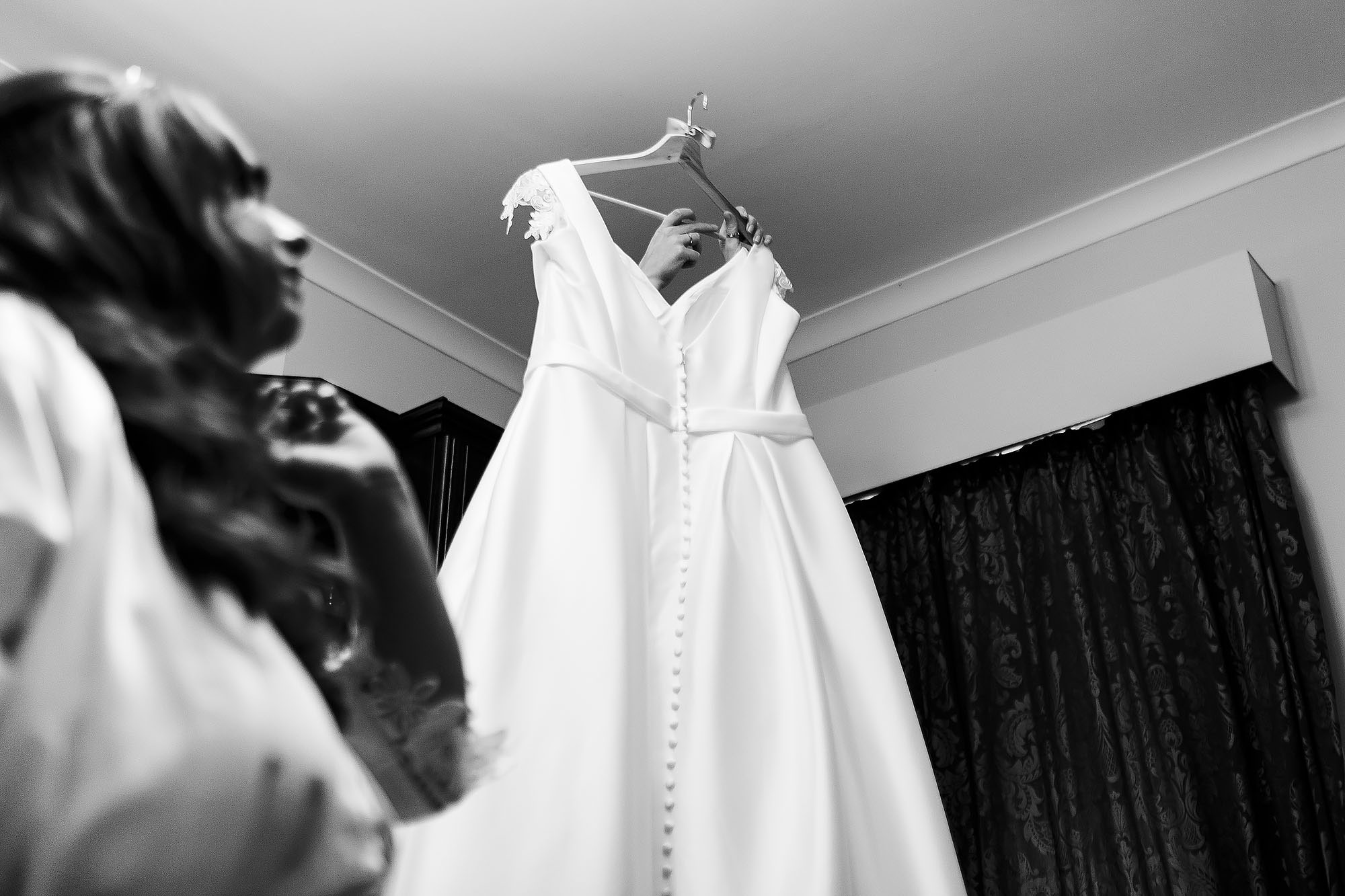 Bride looking up as bridesmaid reaches to the top of the wardrobe to lift down wedding dress | Wellbeing Farm wedding photographs by Toni Darcy Photography