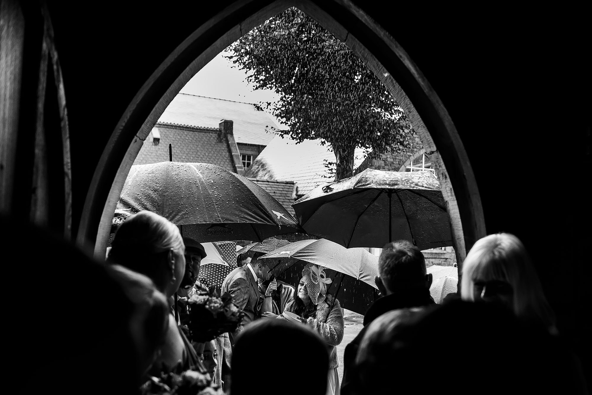 Wedding guests shielding from the rain outside St James the Less Rawtenstall | Wellbeing Farm wedding photographs by Toni Darcy Photography