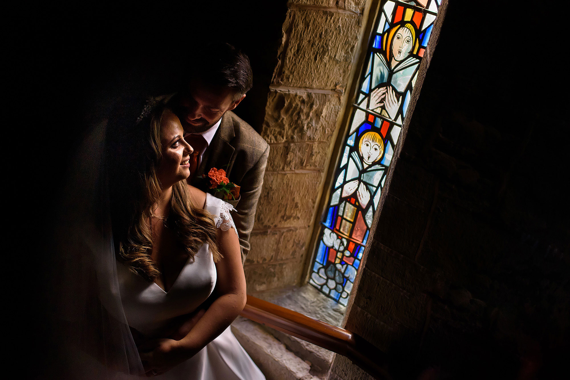 Groom holding bride in his arms close to stained glass window in beautiful light at St James the Less | Wellbeing Farm wedding photographs by Toni Darcy Photography